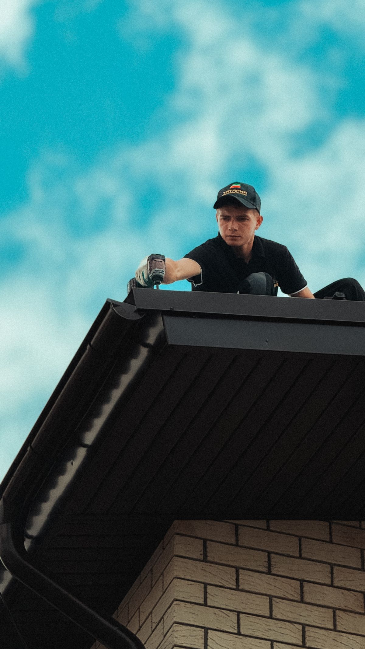 Roofer working on the edge of a dark shingled roof
